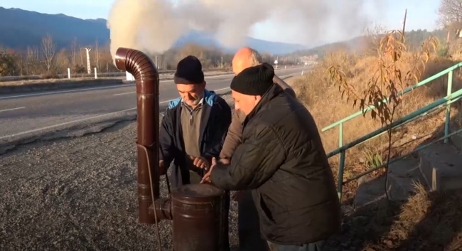 Ekmek almak için bekledikleri durakta seyyar soba ile ısınıyorlar